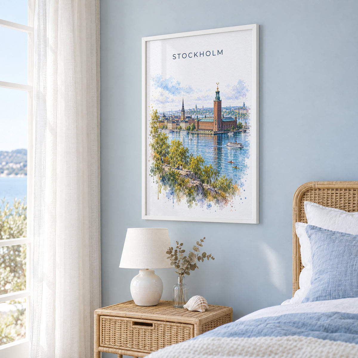 Stockholm watercolor print in a white frame on a pale blue wall beside a rattan bed in a coastal bedroom