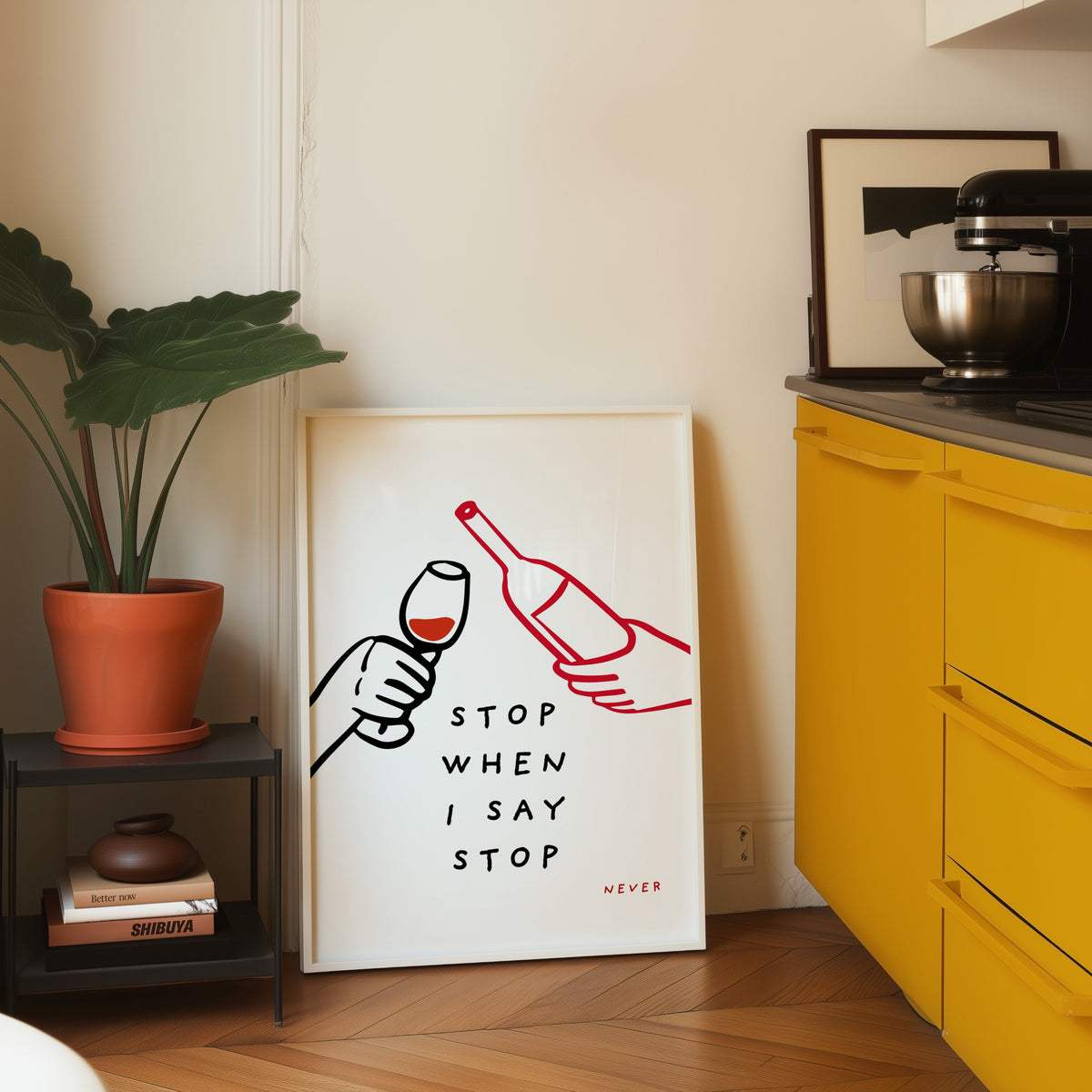 Stop When I Say Stop print in a white frame leaning on parquet beside a bright yellow kitchen