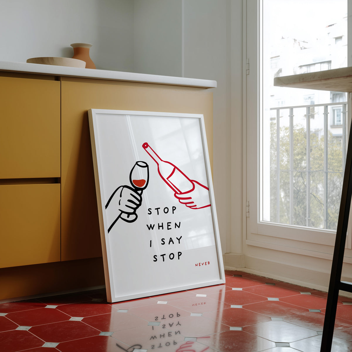 Stop When I Say Stop print in a white frame against yellow cabinets on a red tiled floor