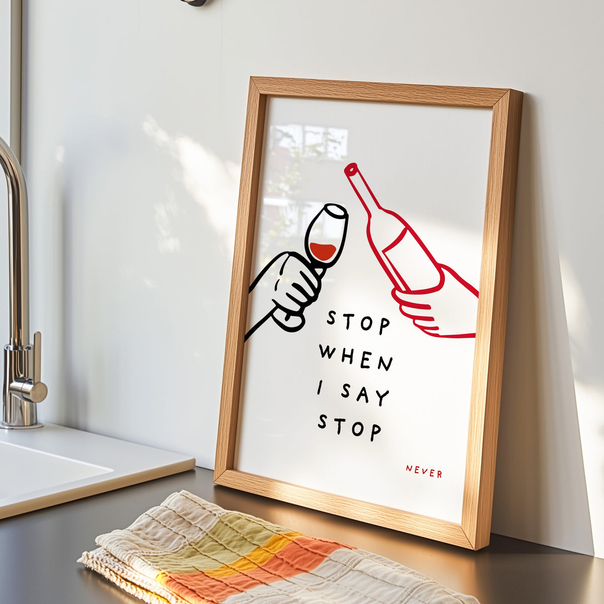 Stop When I Say Stop print in an oak frame by the kitchen sink beside a striped tea towel