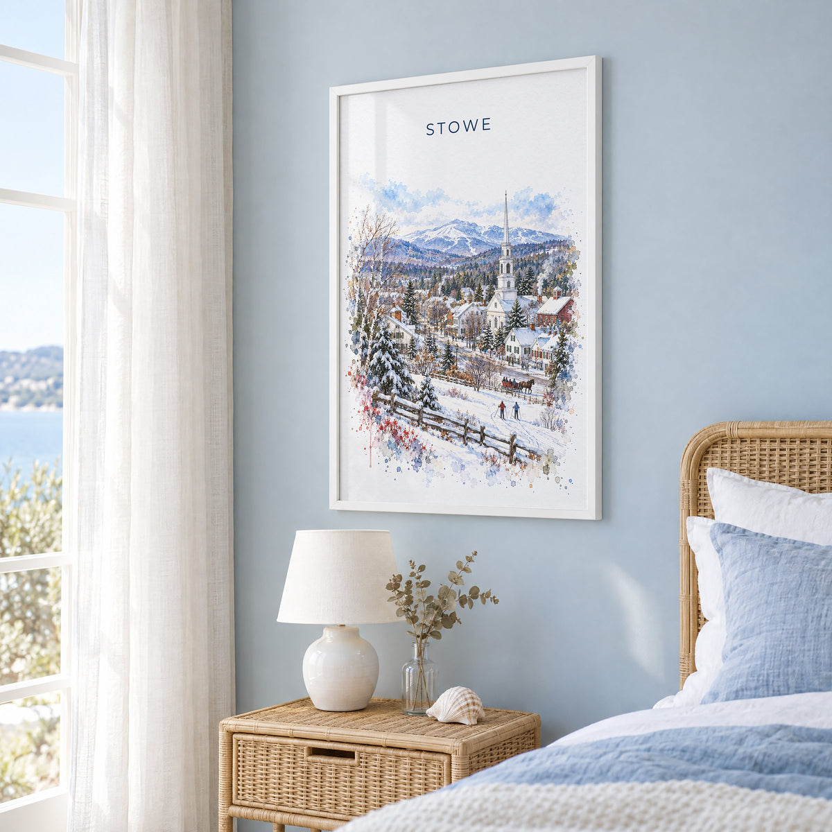 Stowe, Vermont watercolor print in a white frame on a pale blue wall beside a rattan bed in a coastal bedroom