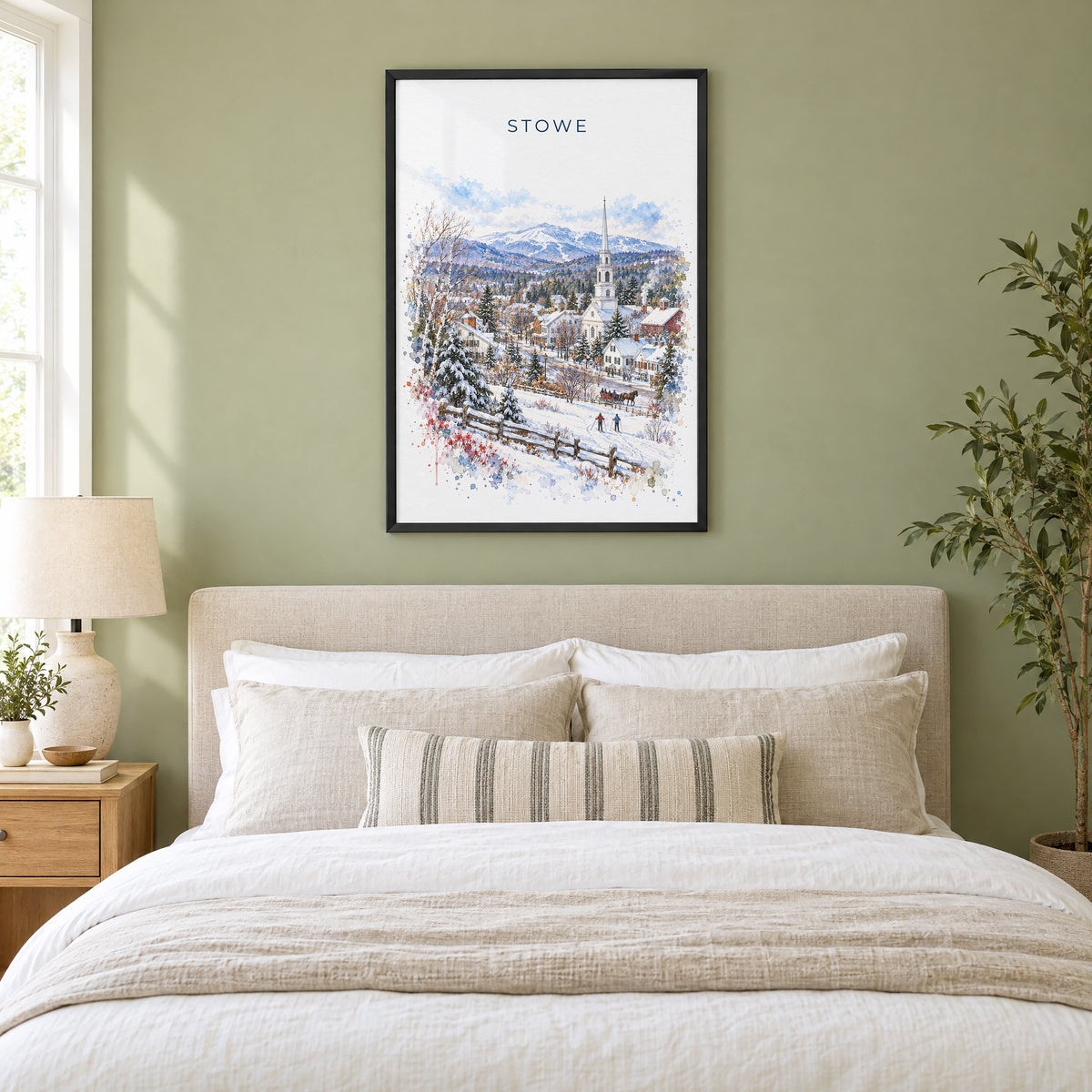 Stowe, Vermont watercolor print in a black frame above an upholstered headboard in a sage green bedroom