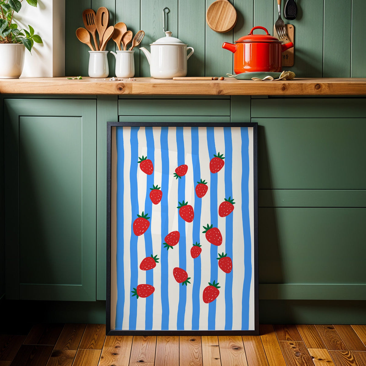 Strawberries blue stripe print in a black frame against sage green kitchen cabinets