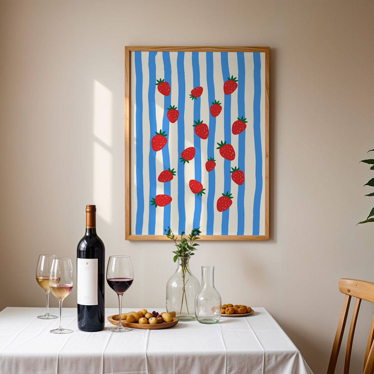 Strawberries blue stripe print in an oak frame above a table laid with red wine