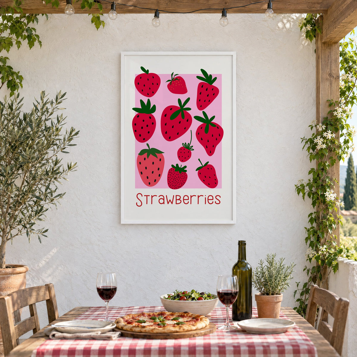 Strawberries thin lettering pink panel berry print in a white frame on a stucco wall above a checked-cloth table with pizza and red wine