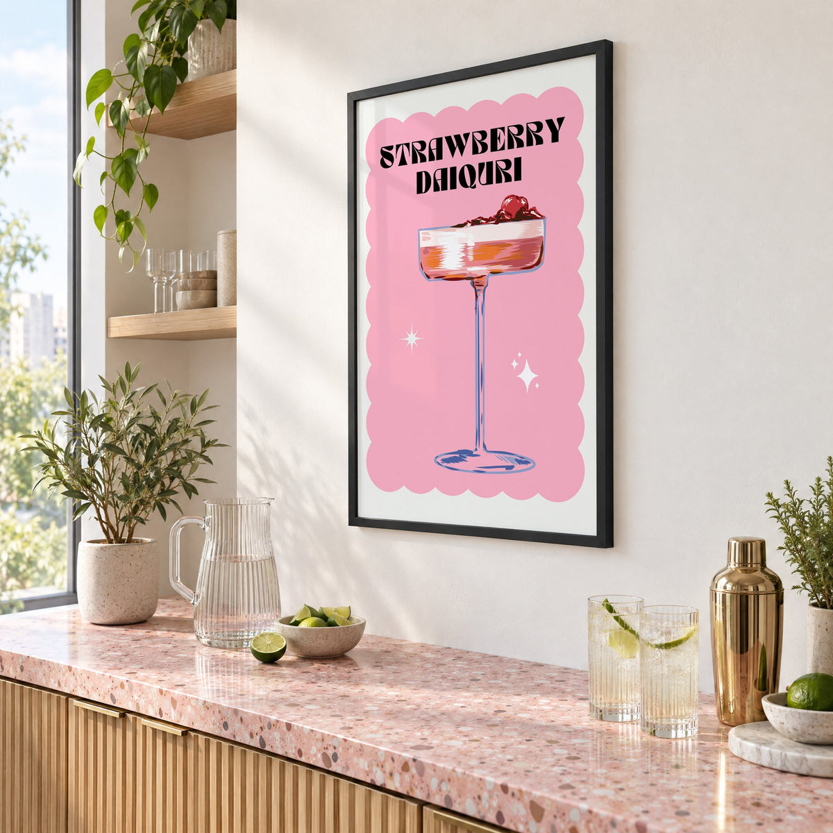 Strawberry daiquiri pink coupe print in a black frame above a pink terrazzo cocktail counter with limes, seen at an angle
