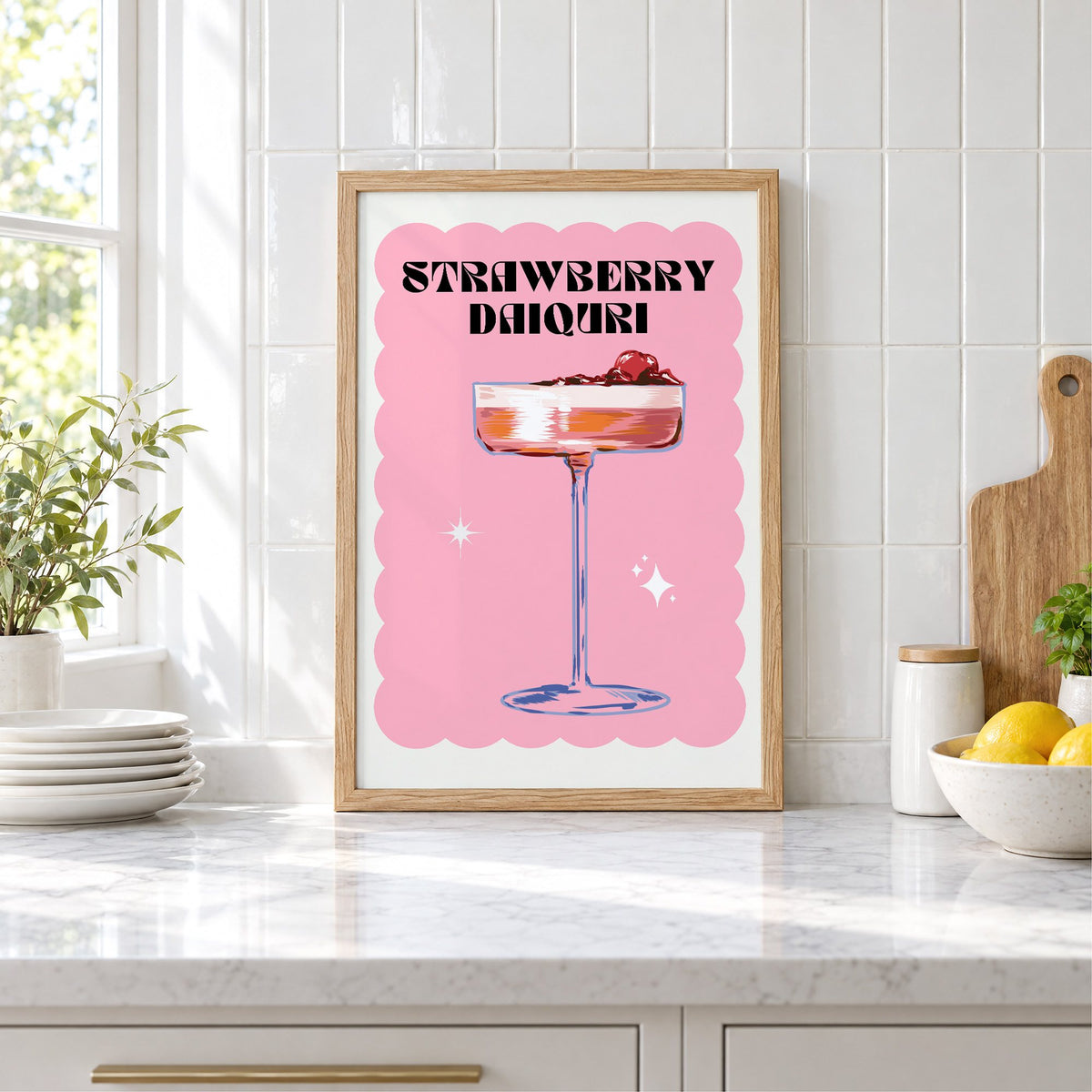 Strawberry daiquiri pink coupe print in an oak frame leaning on a marble counter by white tiles and lemons
