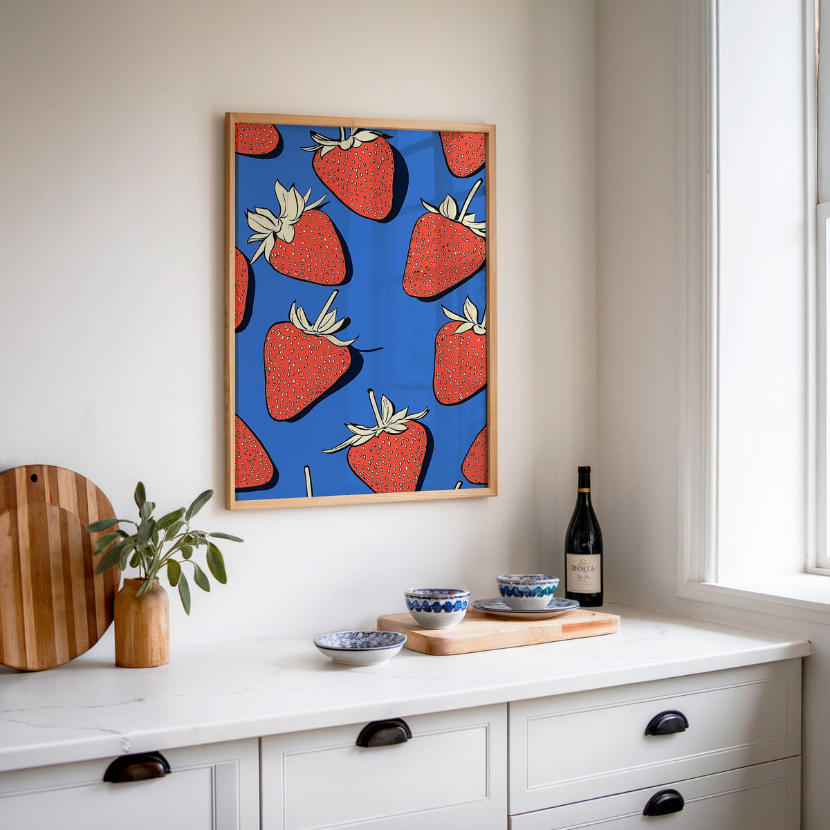 Strawberry pattern print in an oak frame above a white sideboard with a bottle of wine
