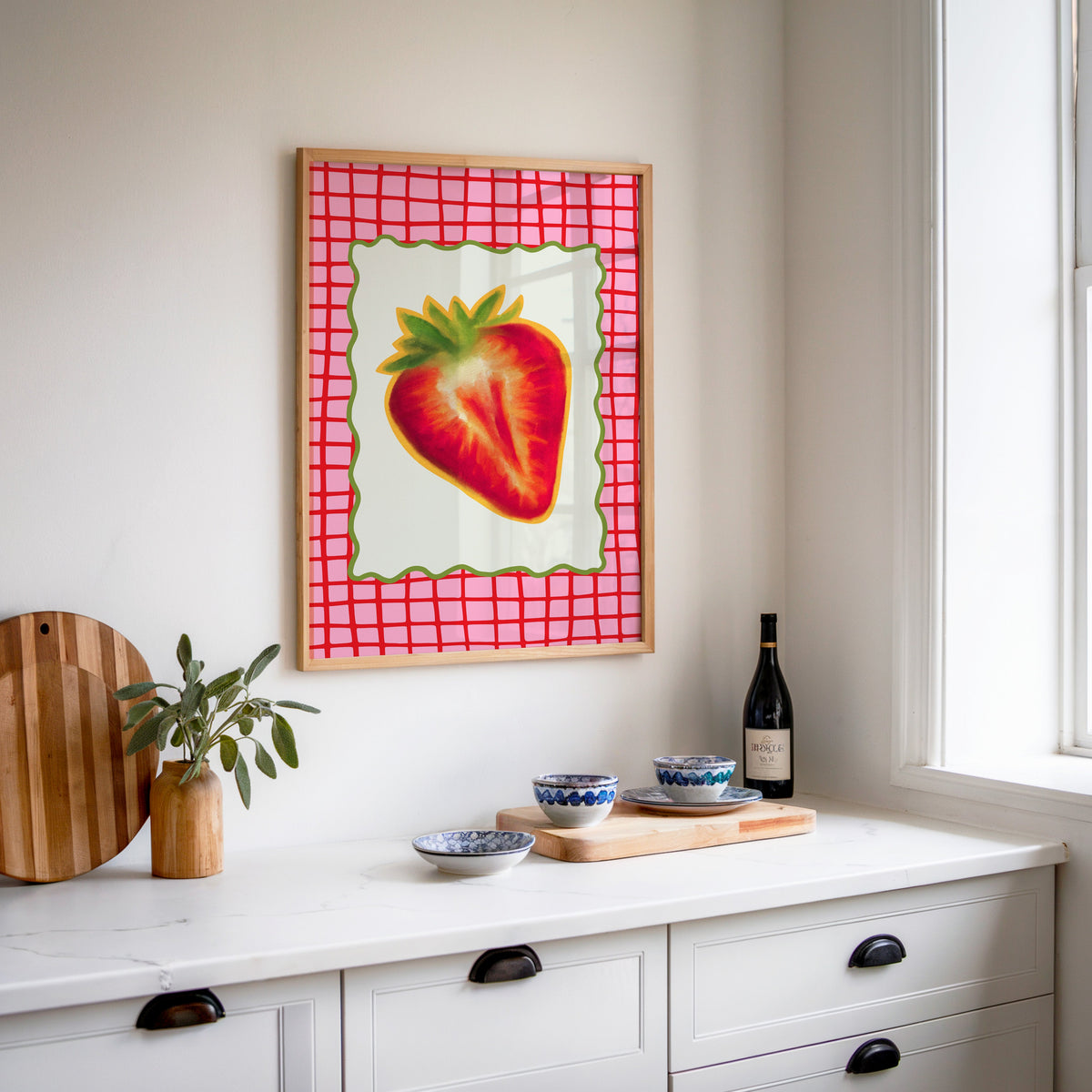 Strawberry red grid print in an oak frame above a white sideboard with a bottle of wine