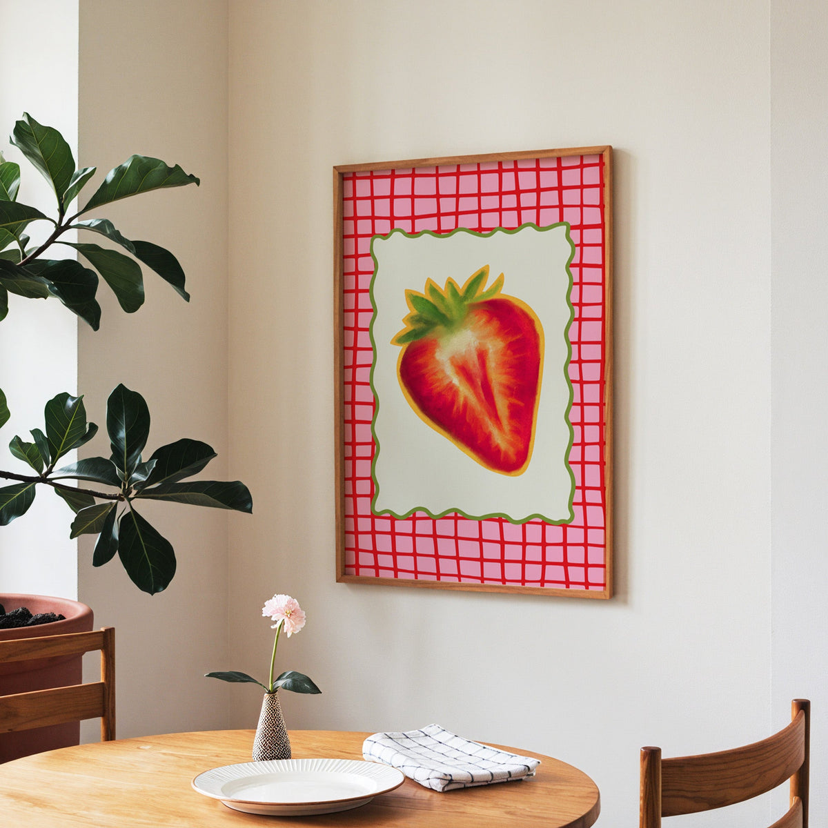 Strawberry red grid print in a walnut frame above a round table beside a fiddle-leaf fig