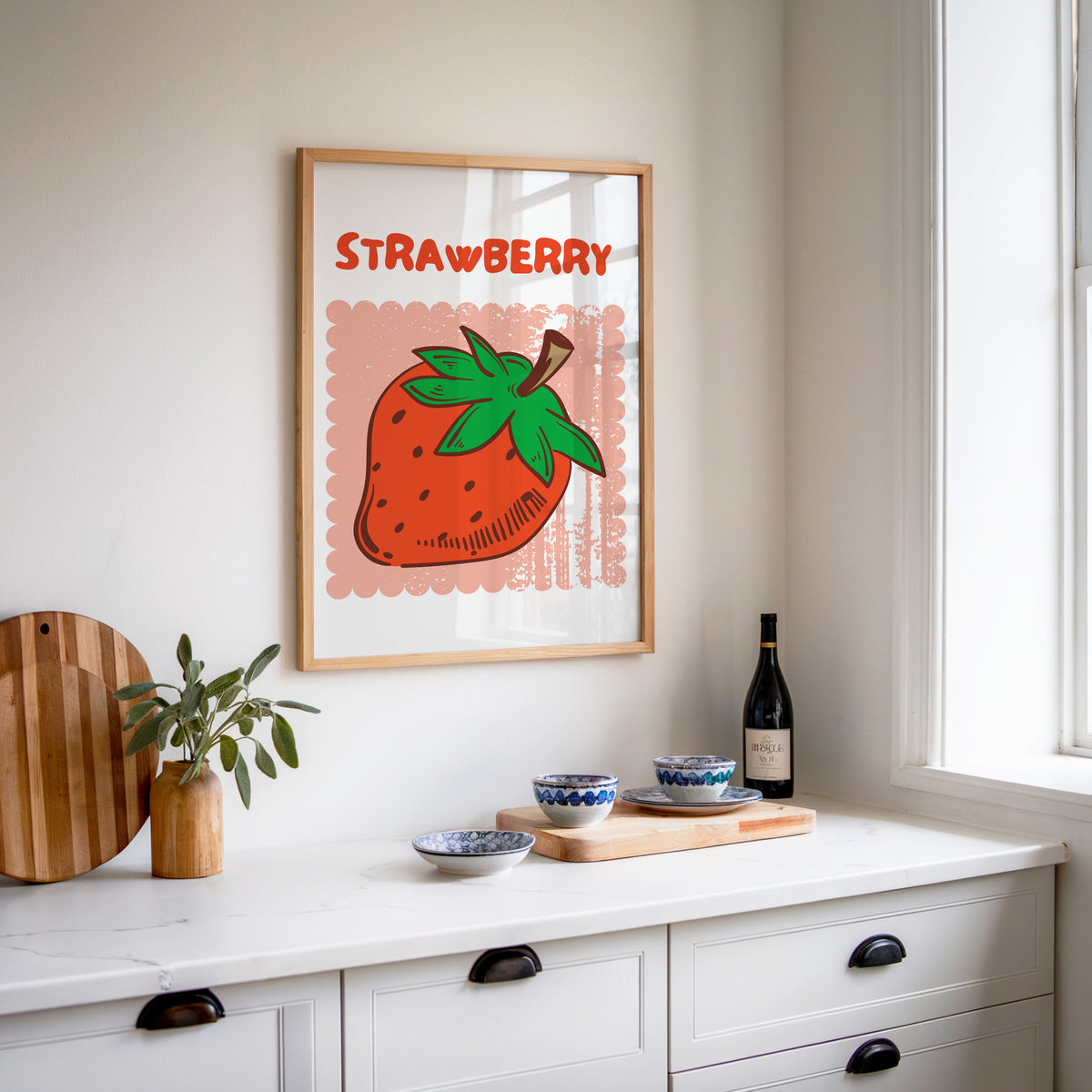 Strawberry scallop print in an oak frame above a white sideboard with a bottle of wine