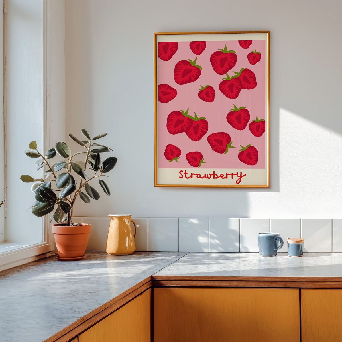 Strawberry print in a gold frame above a marble counter with a yellow ceramic jug