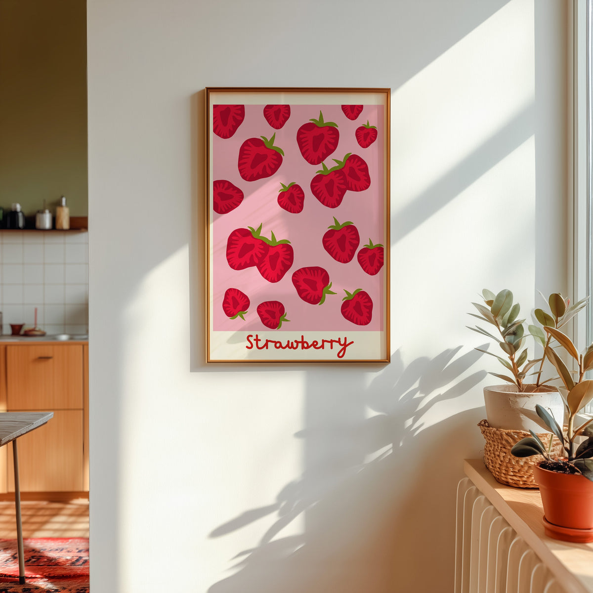 Strawberry print in a gold frame in sunlight with plants and a kitchen beyond