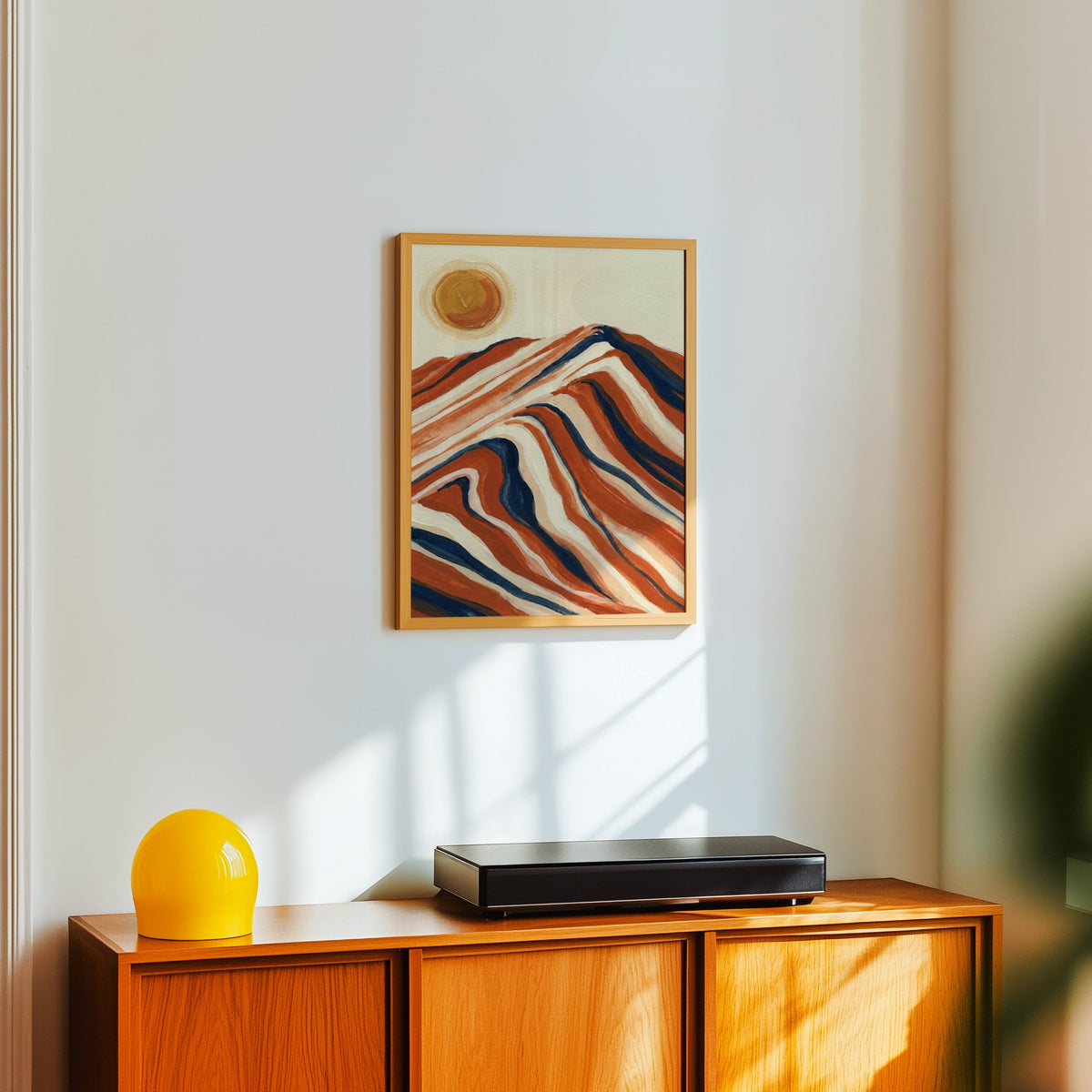 Mid-century mountain print in a light oak frame above a teak sideboard with a yellow lamp