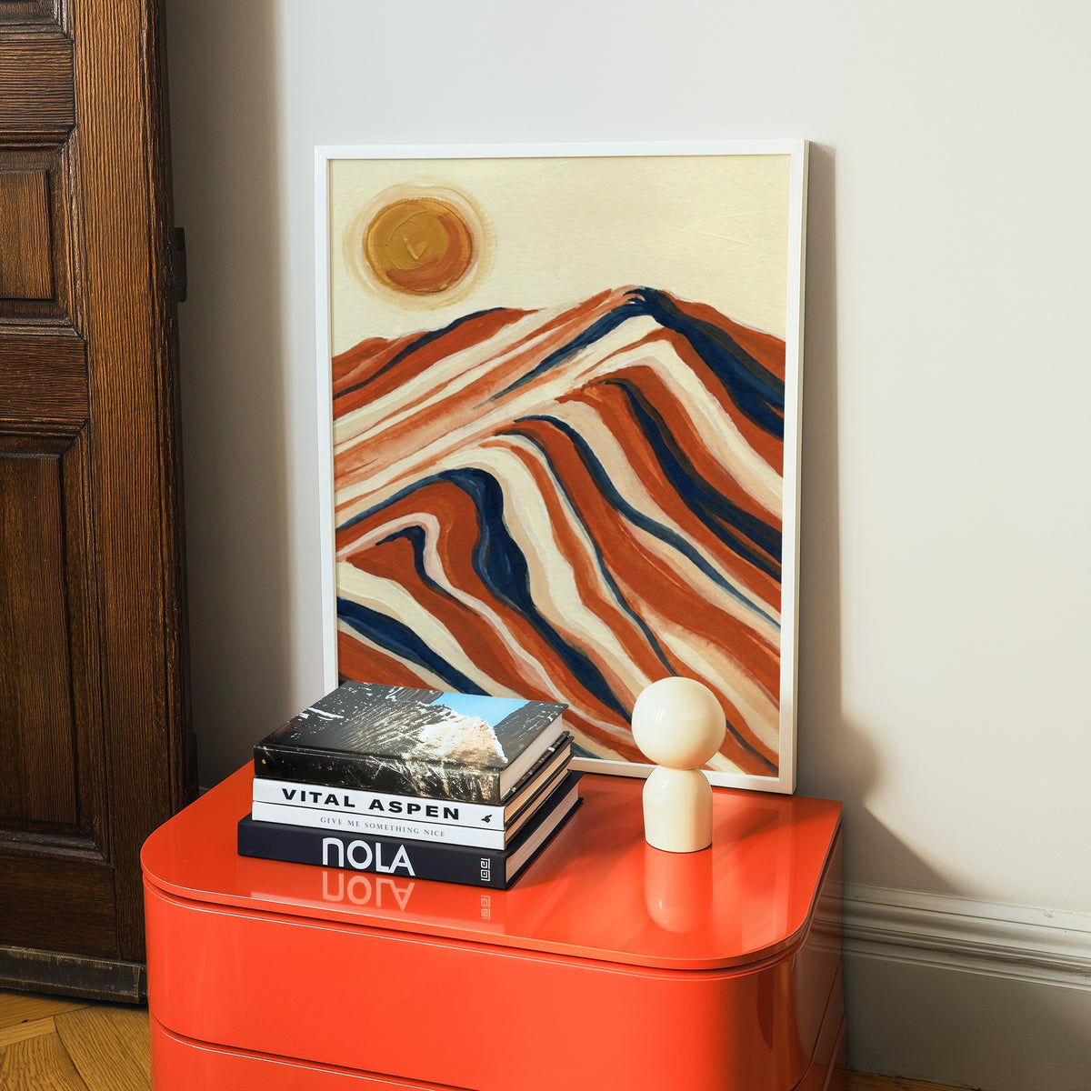 Boho abstract landscape print in a white frame on a glossy orange cabinet with books