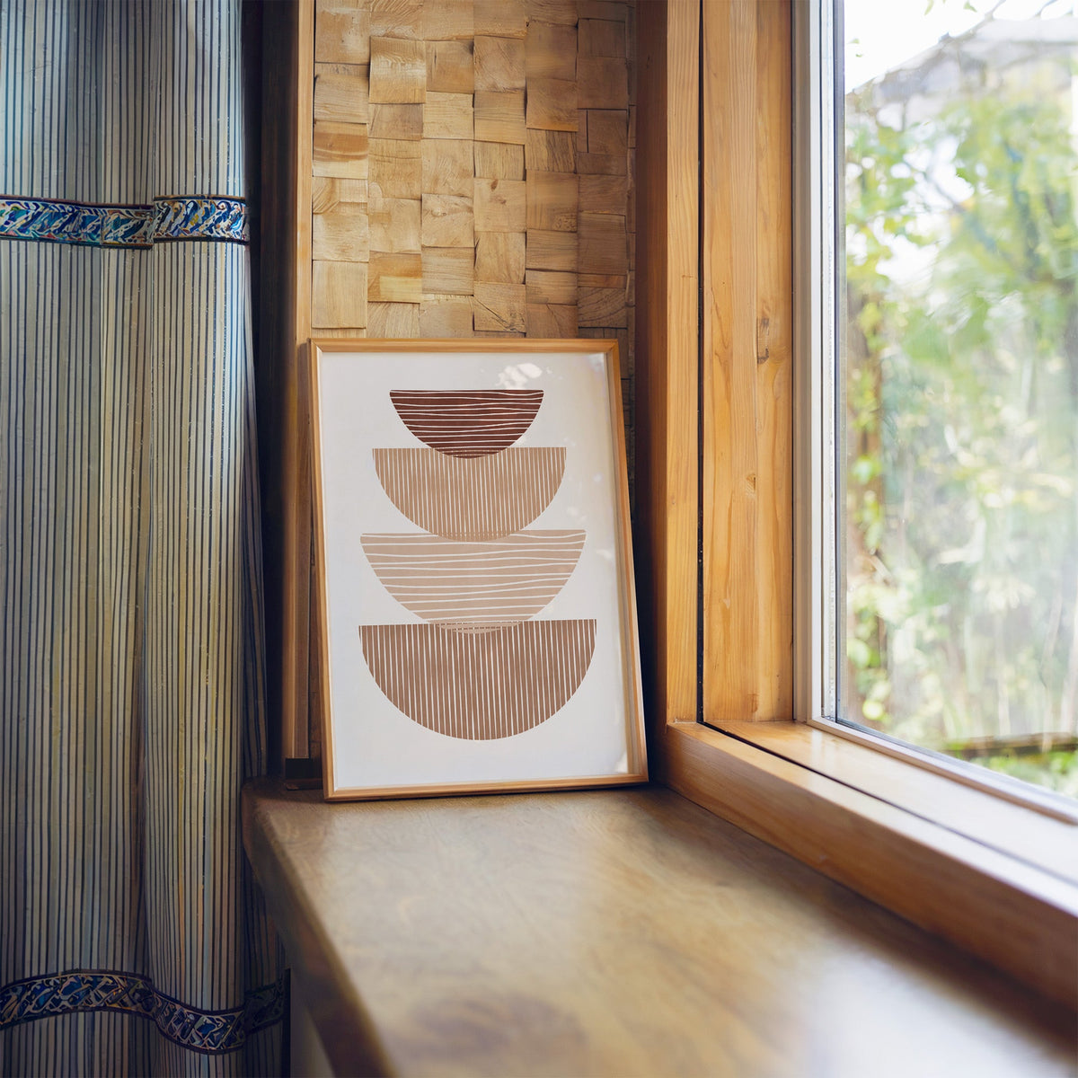 Striped stacked bowls earth tone print in a light wood frame leaning on a wooden window sill by a garden view