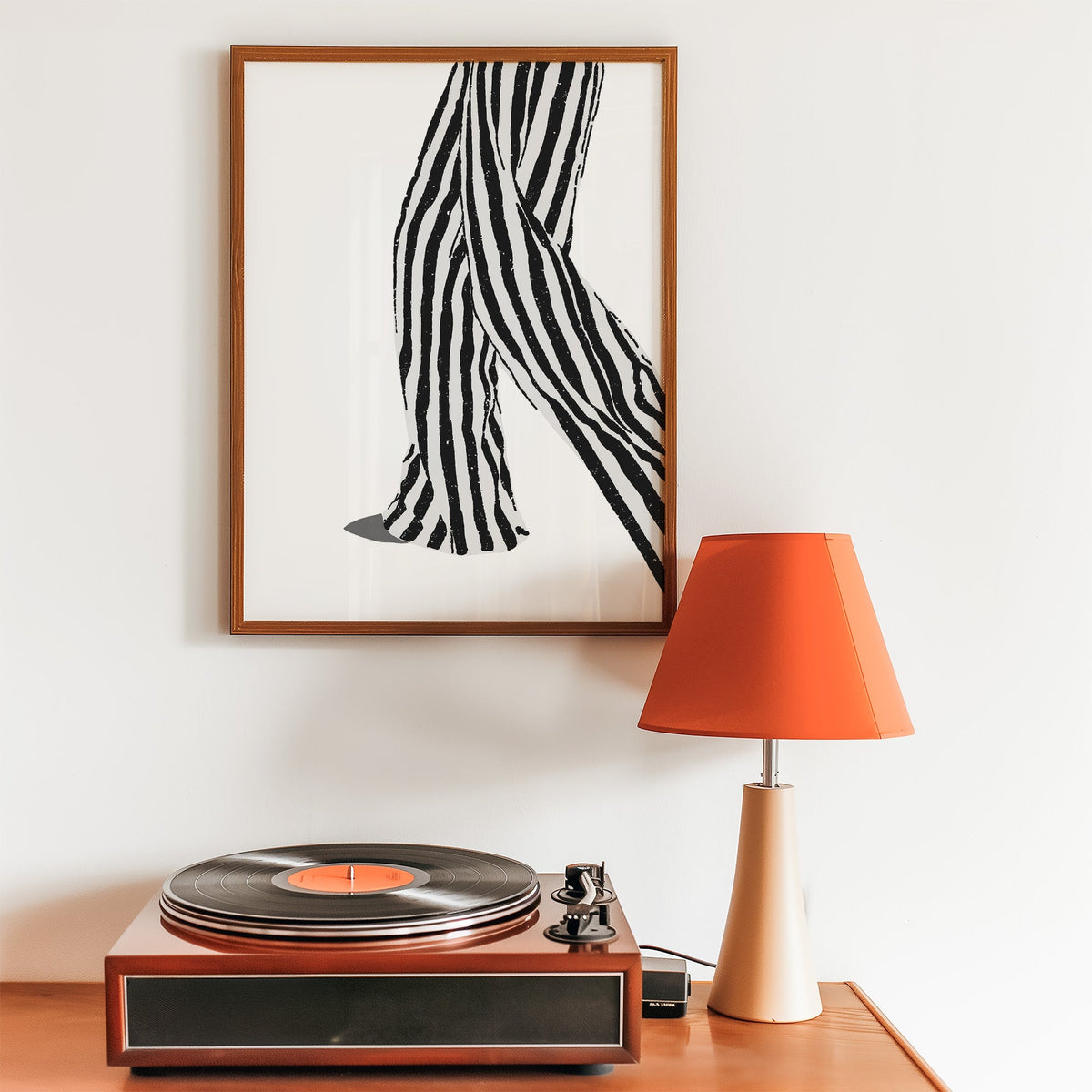Walking legs in striped trousers graphic print in a walnut frame above a record player and orange lamp
