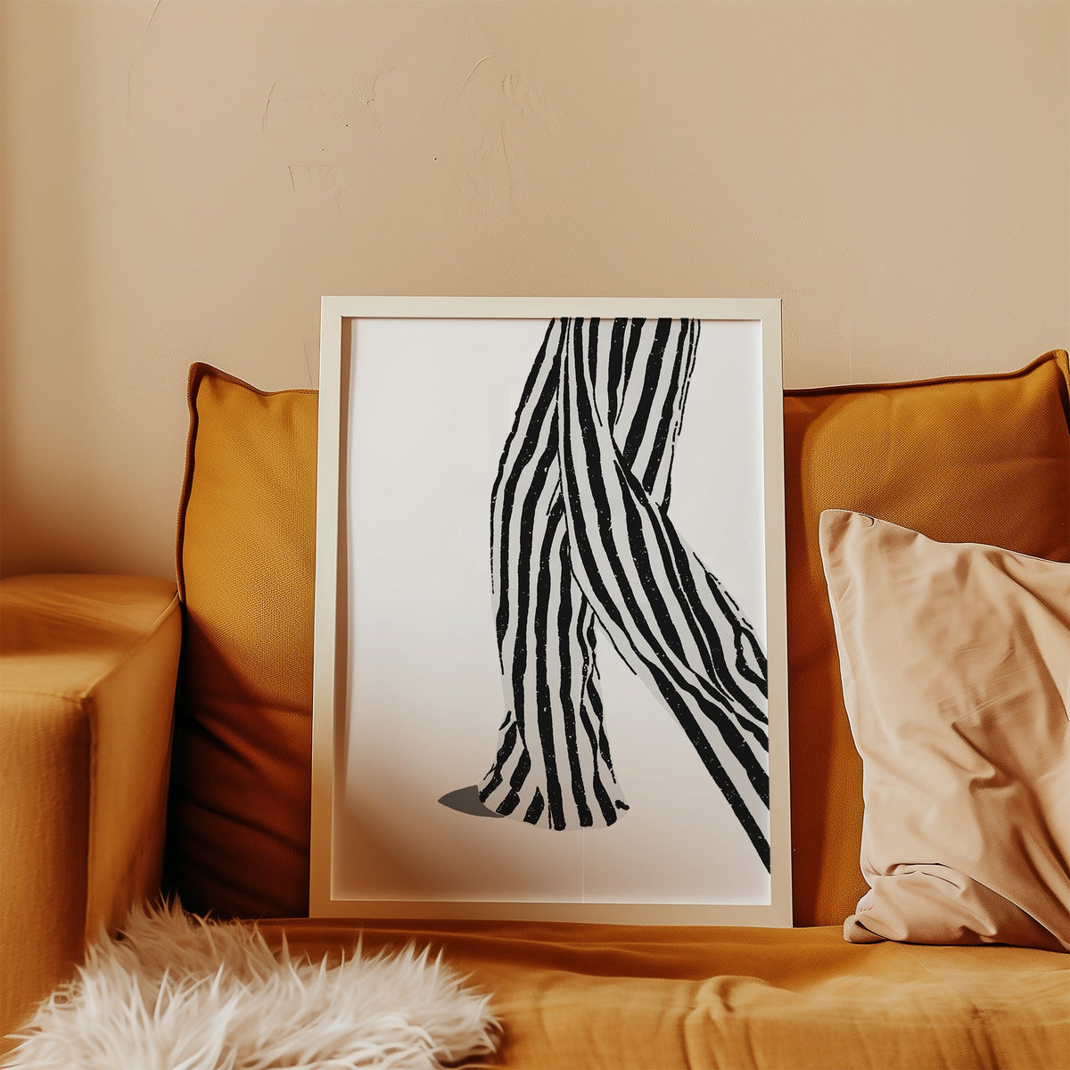 Walking legs in striped trousers graphic print in a white frame leaning on a mustard velvet sofa