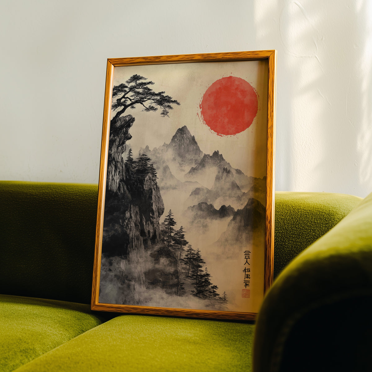 Sumi-e misty mountains and red sun print in an oak frame propped on a green velvet sofa