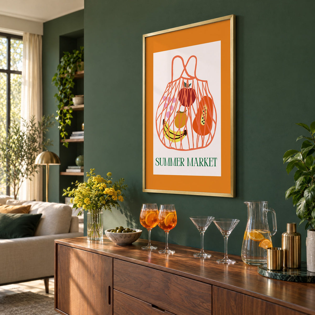 SUMMER MARKET fruit net bag print in a brass frame on a bottle green wall above a sideboard with spritz and martini glasses, seen at an angle
