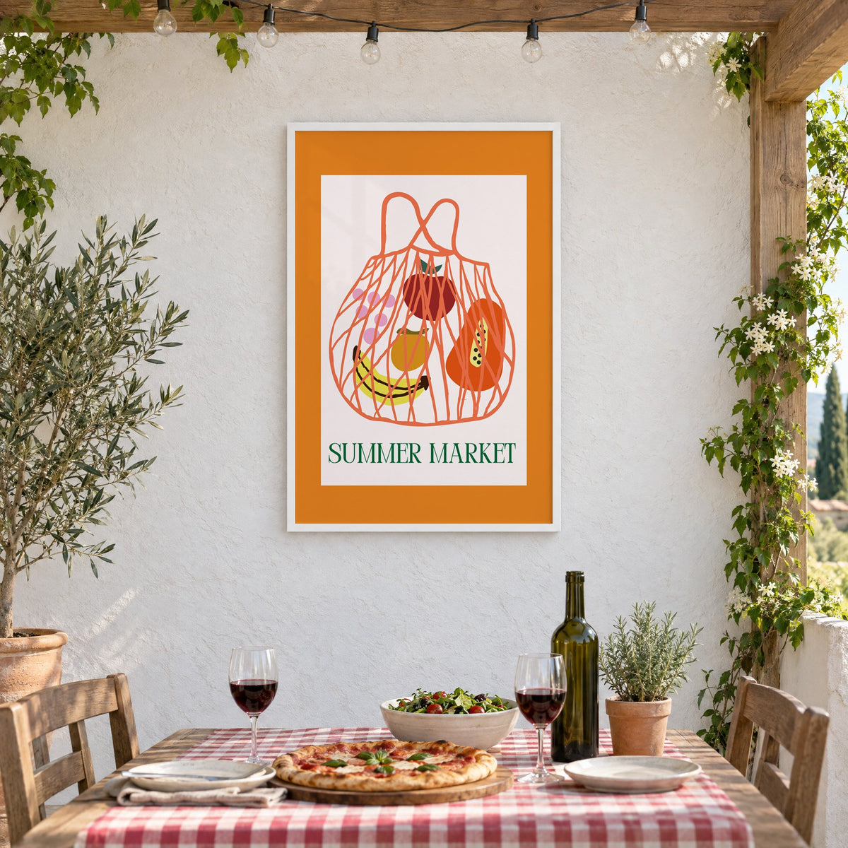SUMMER MARKET fruit net bag print in a white frame on a stucco wall above a checked-cloth table with pizza and red wine