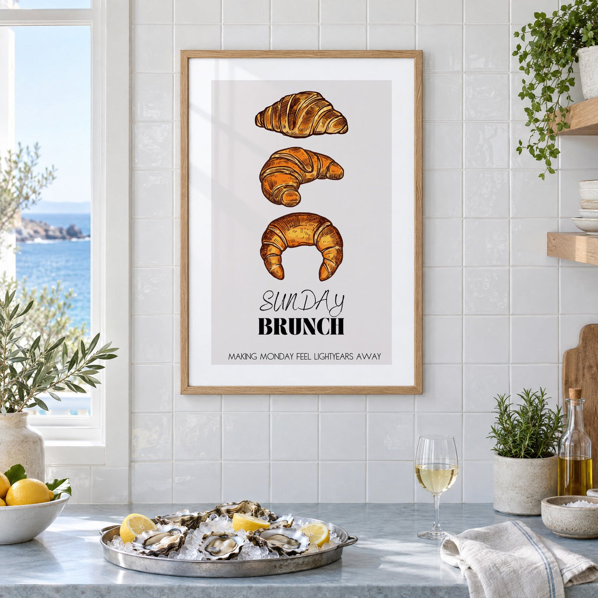 SUNDAY BRUNCH three croissants print in an oak frame on white tiles above a marble counter with oysters and lemons by a sea view