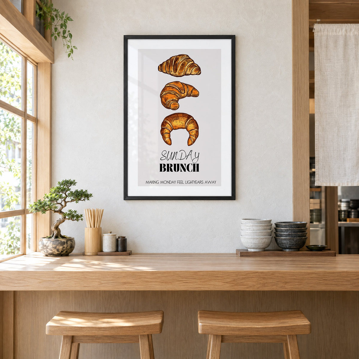 SUNDAY BRUNCH three croissants print in a black frame above a light wood ramen counter with stools and stacked bowls