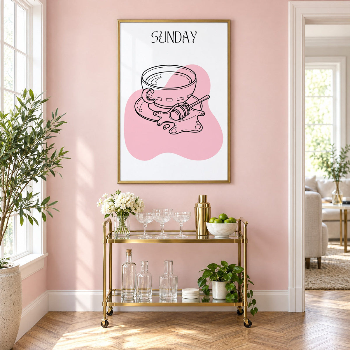 SUNDAY teacup and honey dipper line print in a brass frame on a blush pink wall above a gold bar cart with glassware