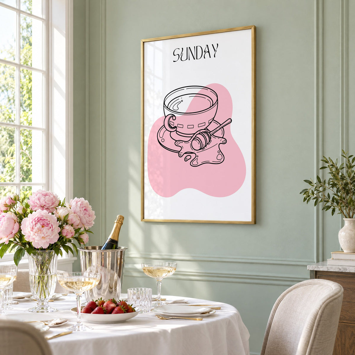 SUNDAY teacup and honey dipper line print in a brass frame on a sage wall above a brunch table with champagne and peonies, seen at an angle