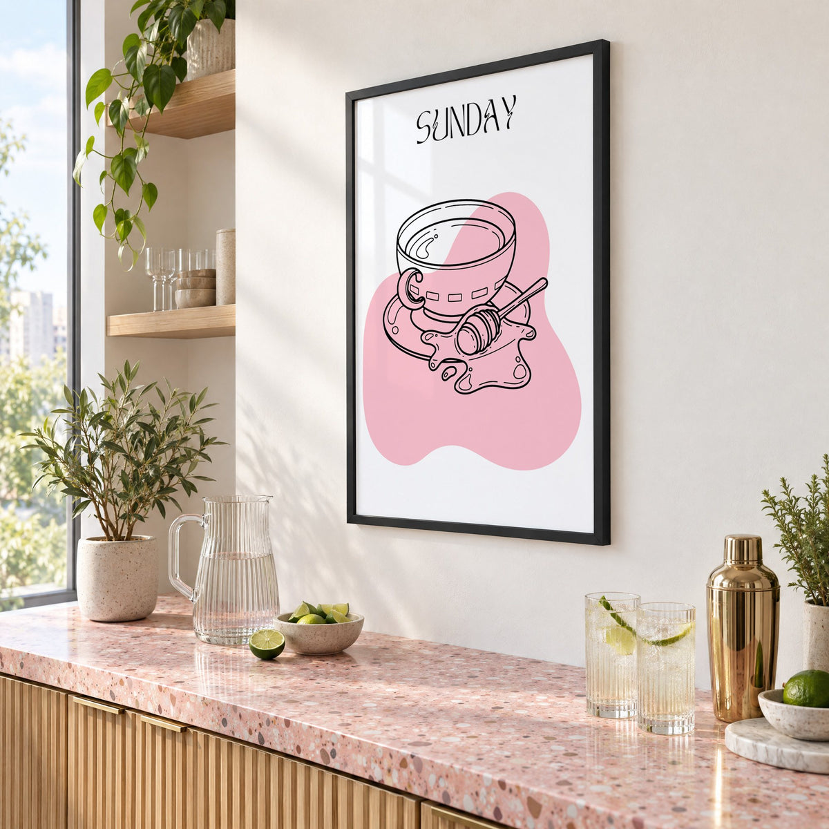 SUNDAY teacup and honey dipper line print in a black frame above a pink terrazzo cocktail counter with limes, seen at an angle