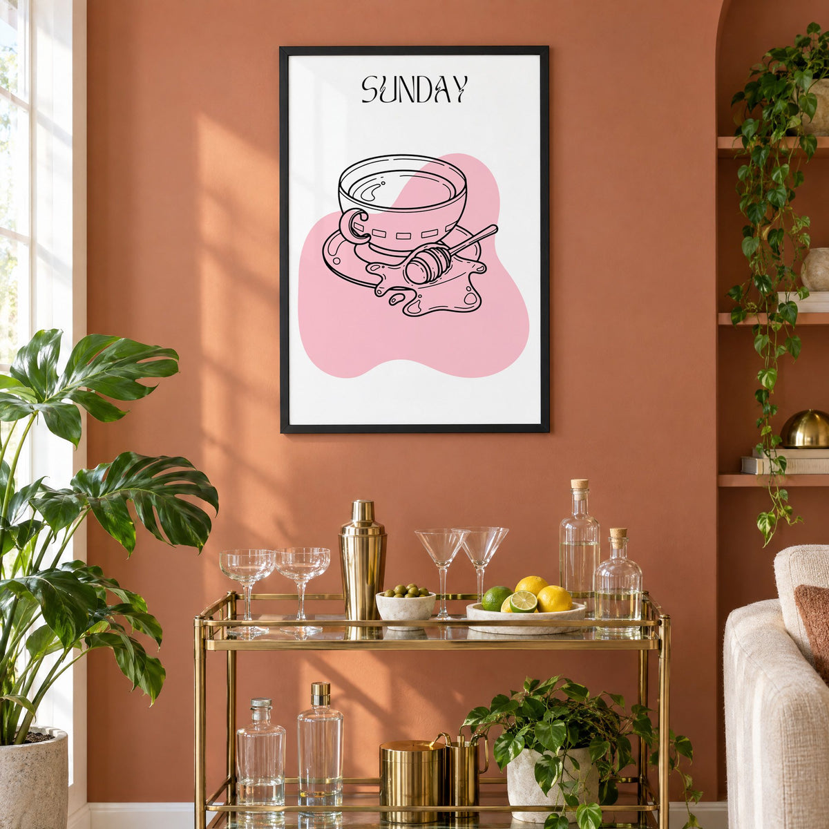 SUNDAY teacup and honey dipper line print in a black frame on a terracotta wall above a brass bar cart with coupes and citrus