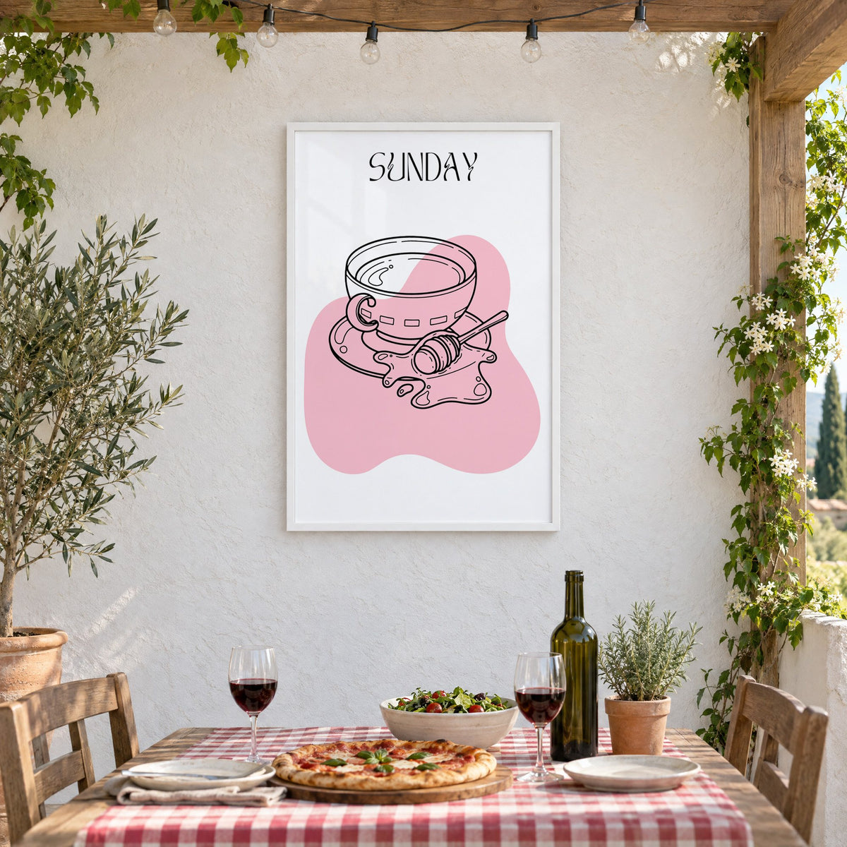 SUNDAY teacup and honey dipper line print in a white frame on a stucco wall above a checked-cloth table with pizza and red wine