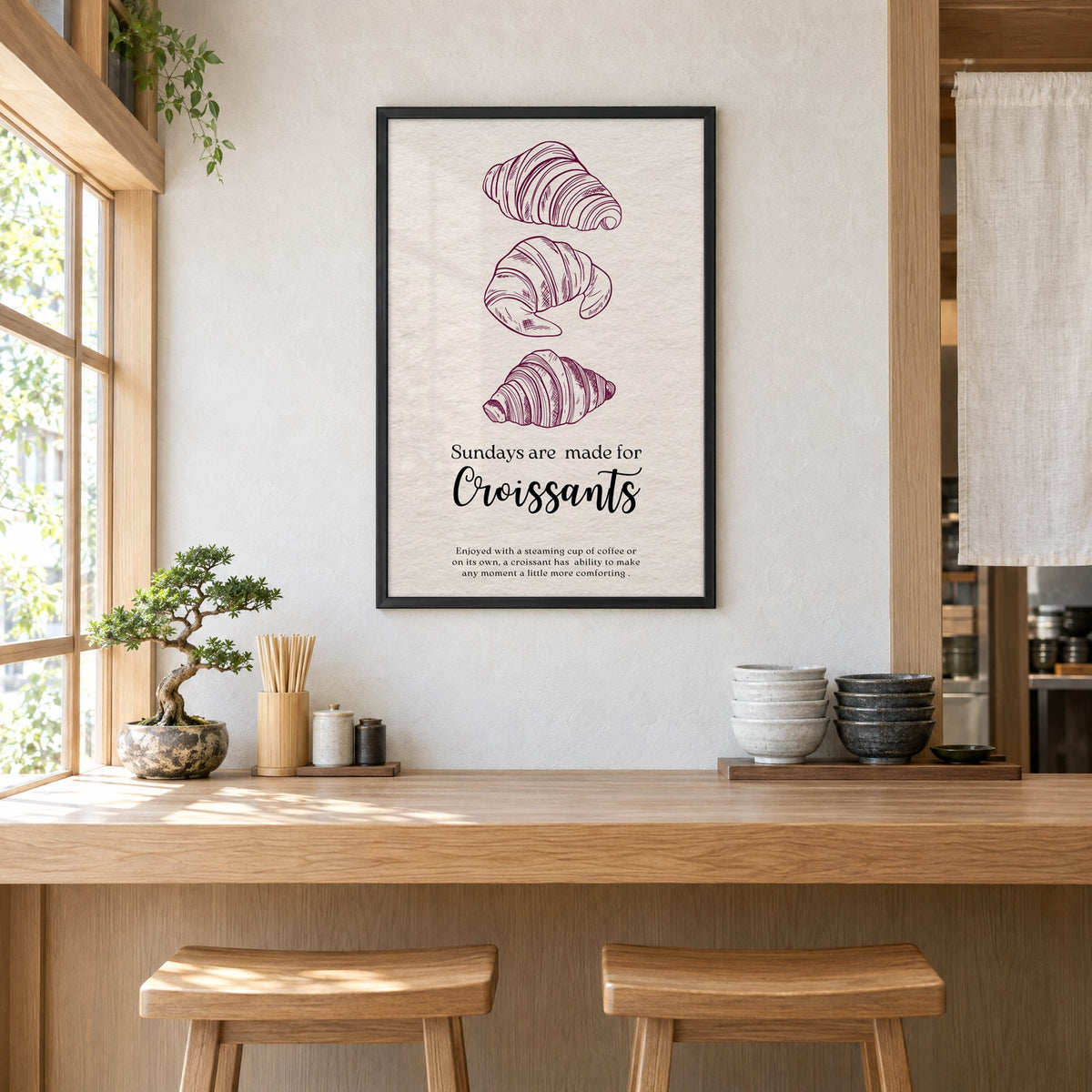Sundays are made for Croissants burgundy engraving print in a black frame above a light wood ramen counter with stools and stacked bowls