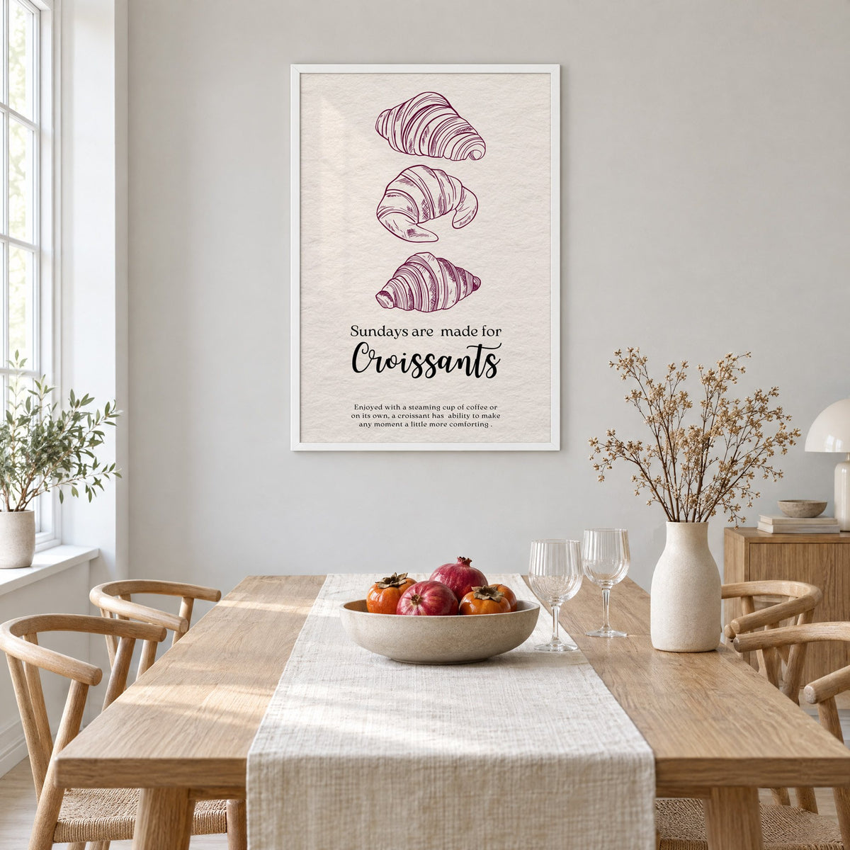 Sundays are made for Croissants burgundy engraving print in a white frame above a light oak dining table with a linen runner and fruit bowl