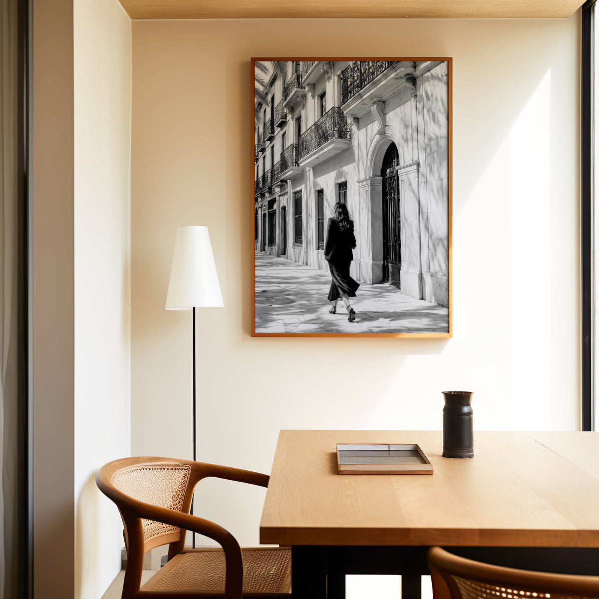 Black and white woman walking under iron balconies print in an oak frame above a dining table and cane chair