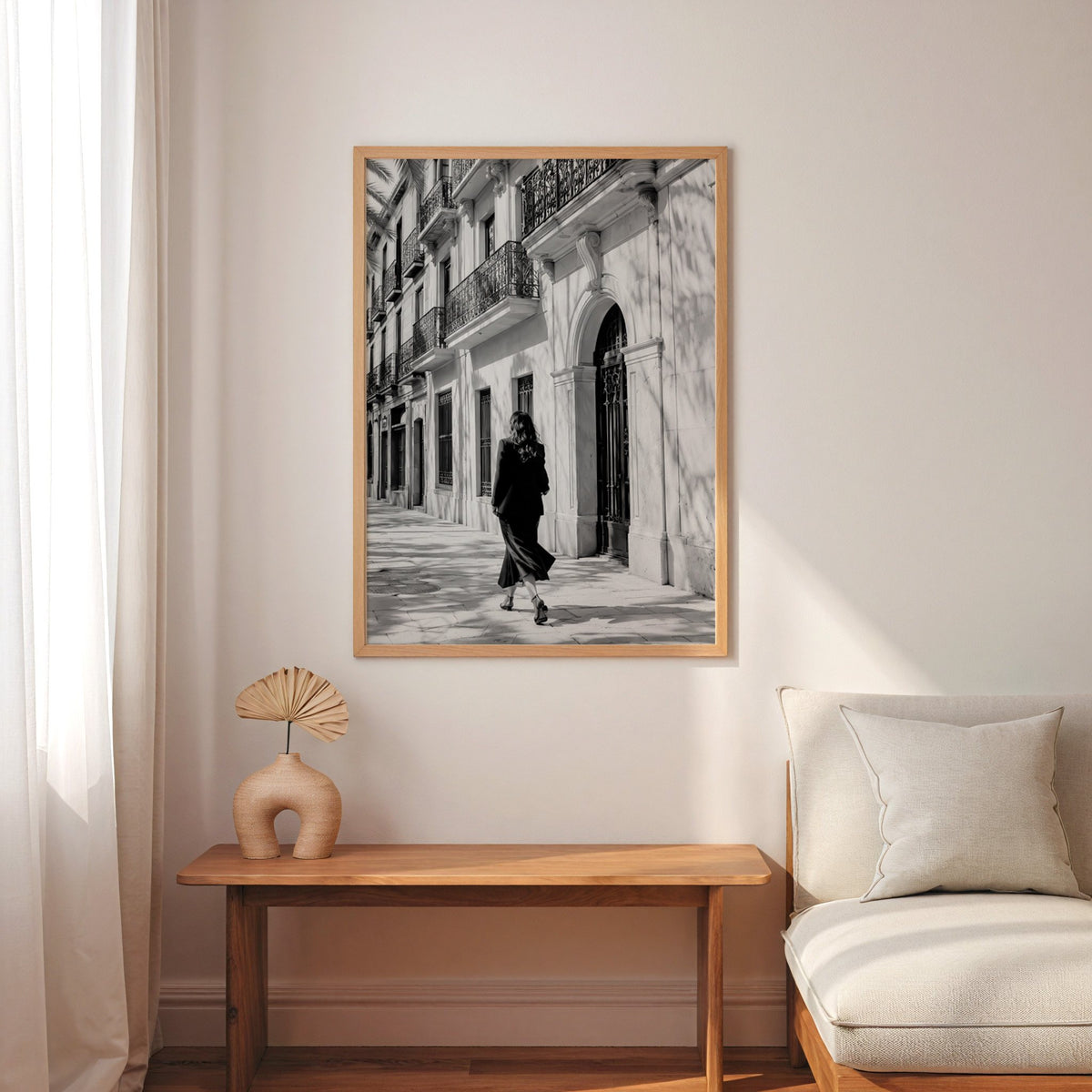 Black and white woman walking under iron balconies print in an oak frame above a narrow console with an arched vase