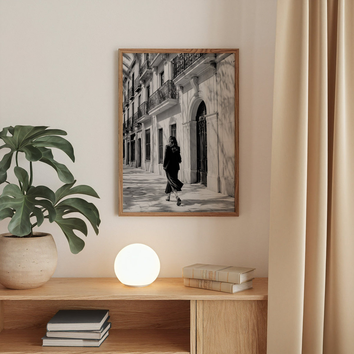 Black and white woman walking under iron balconies print in a walnut frame above an oak cabinet with a glowing globe lamp