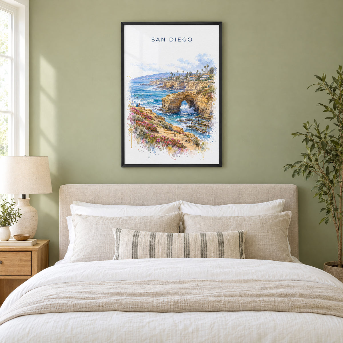 Sunset Cliffs San Diego watercolor print in a black frame above an upholstered headboard in a sage green bedroom