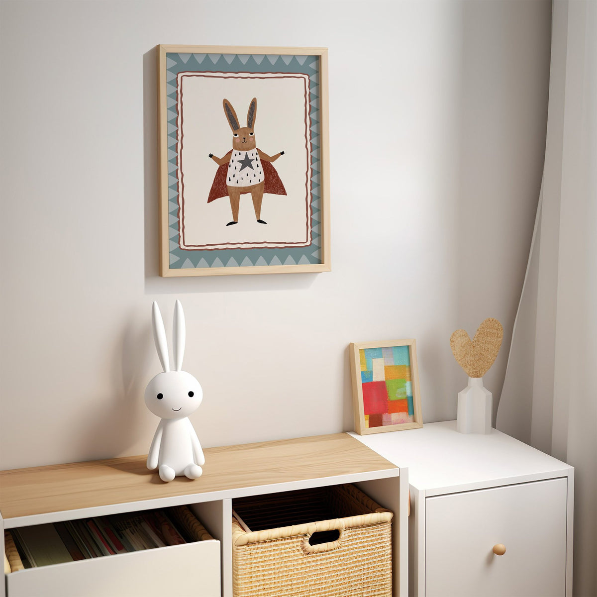 Superhero bunny in red cape nursery print in an oak frame above a kids cubby shelf with a woven basket and bunny lamp