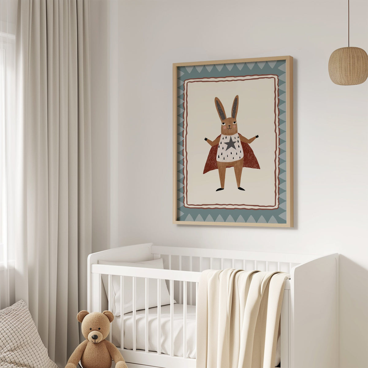 Superhero bunny in red cape nursery print in an oak frame above a white crib with a teddy bear