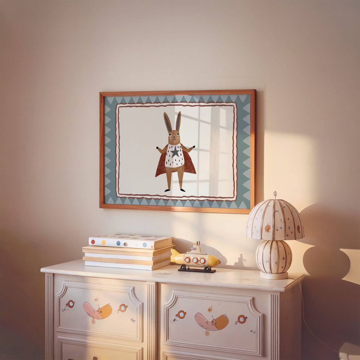 Landscape superhero bunny in red cape nursery print in a cherry wood frame above a painted dresser and lamp