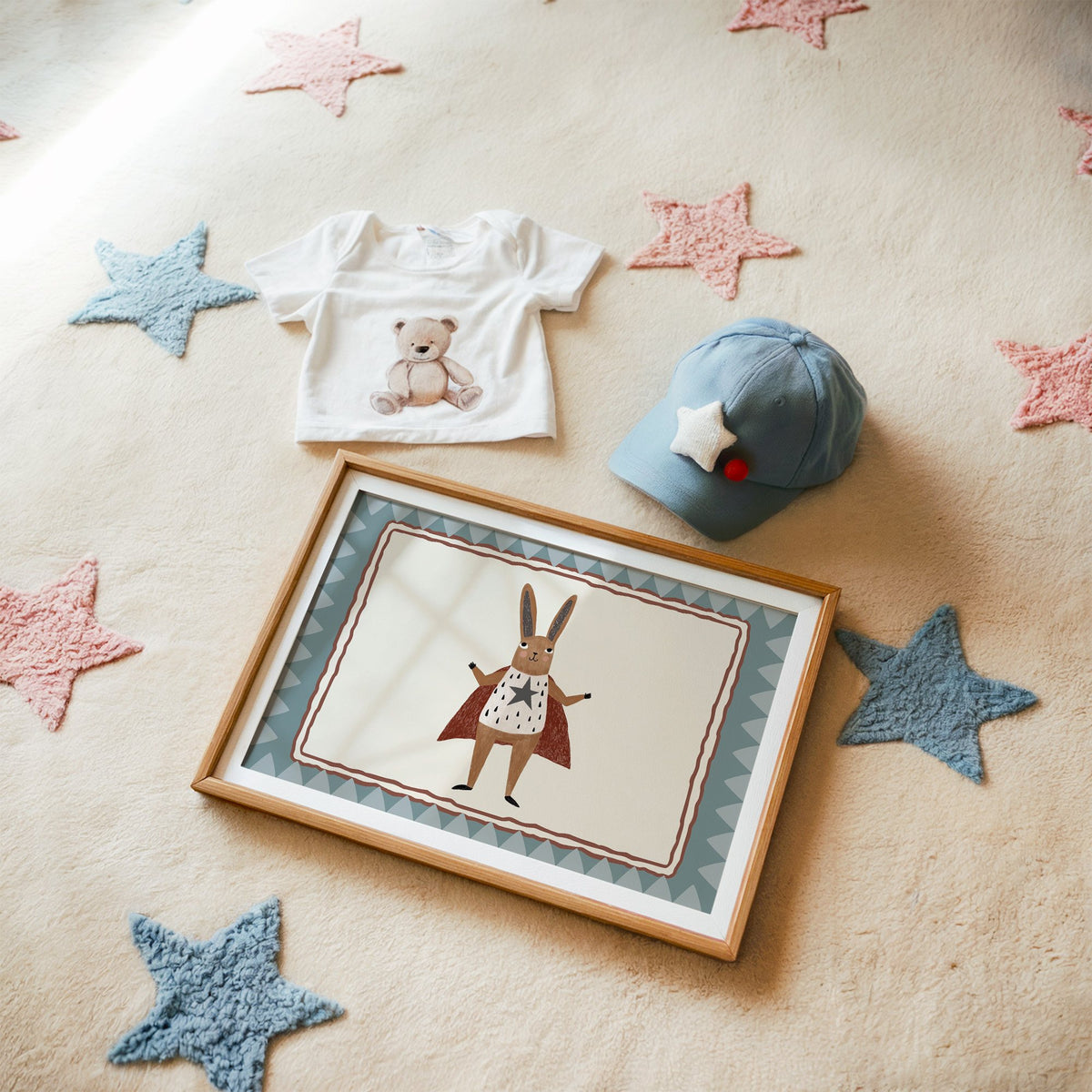 Landscape superhero bunny in red cape nursery print in a matted oak frame on a star rug with a baby tee