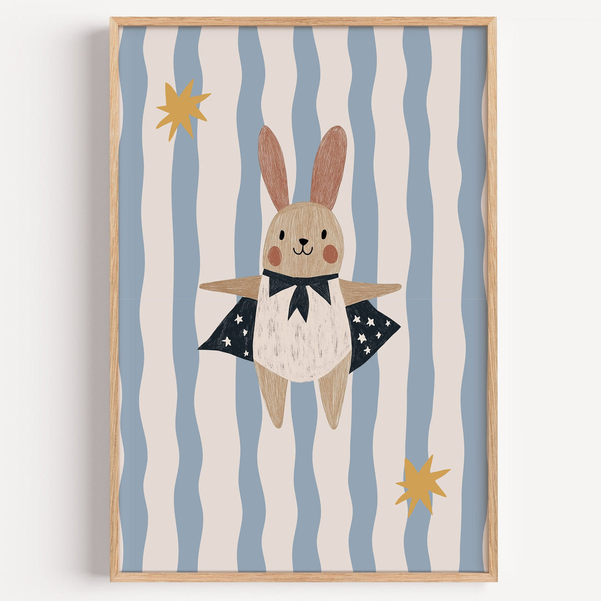 Superhero bunny star cape nursery print in a light oak frame on a plain white wall
