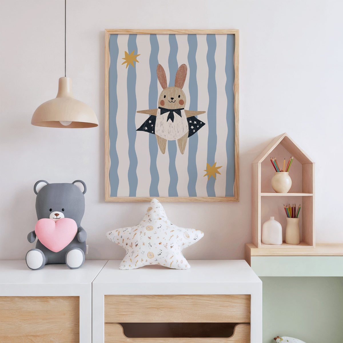 Superhero bunny star cape nursery print in an oak frame above a white dresser with a star pillow and house shelf
