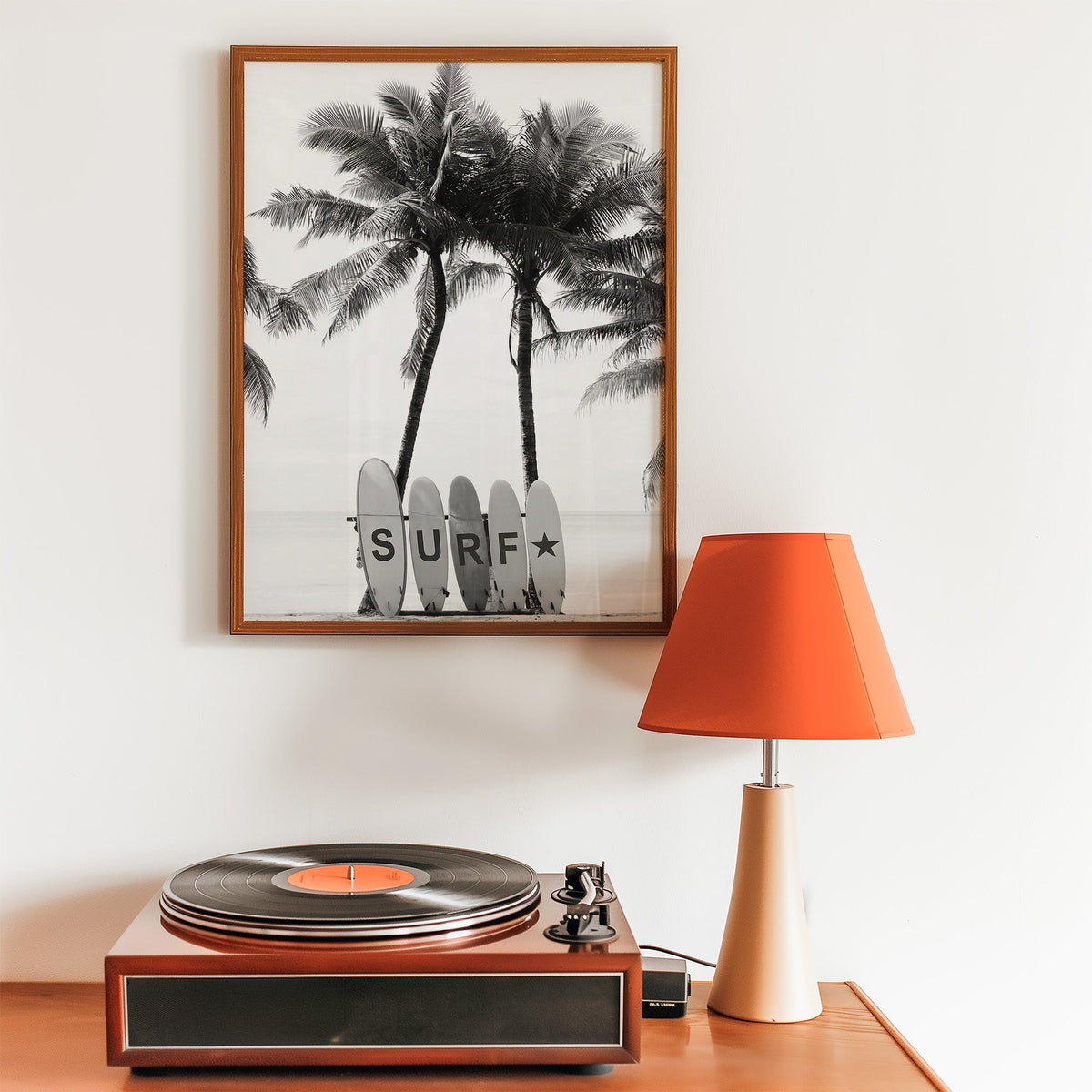Five surfboards spelling SURF under coconut palms print in a walnut frame above a record player and orange lamp