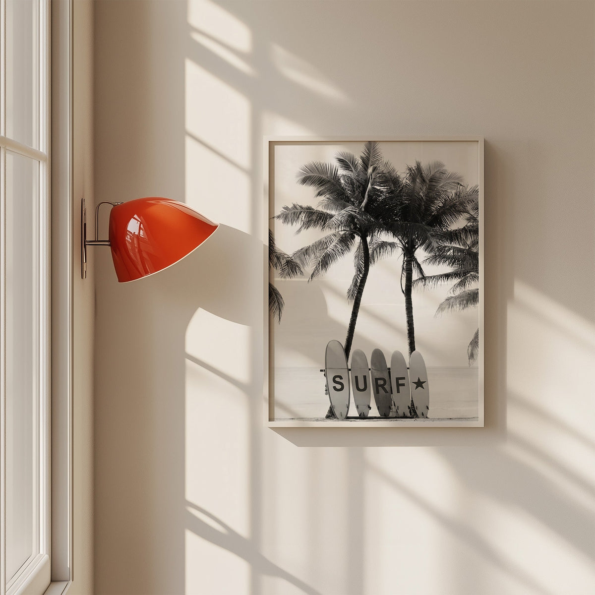 Five surfboards spelling SURF under coconut palms print in a white frame on a sunlit wall beside a red sconce