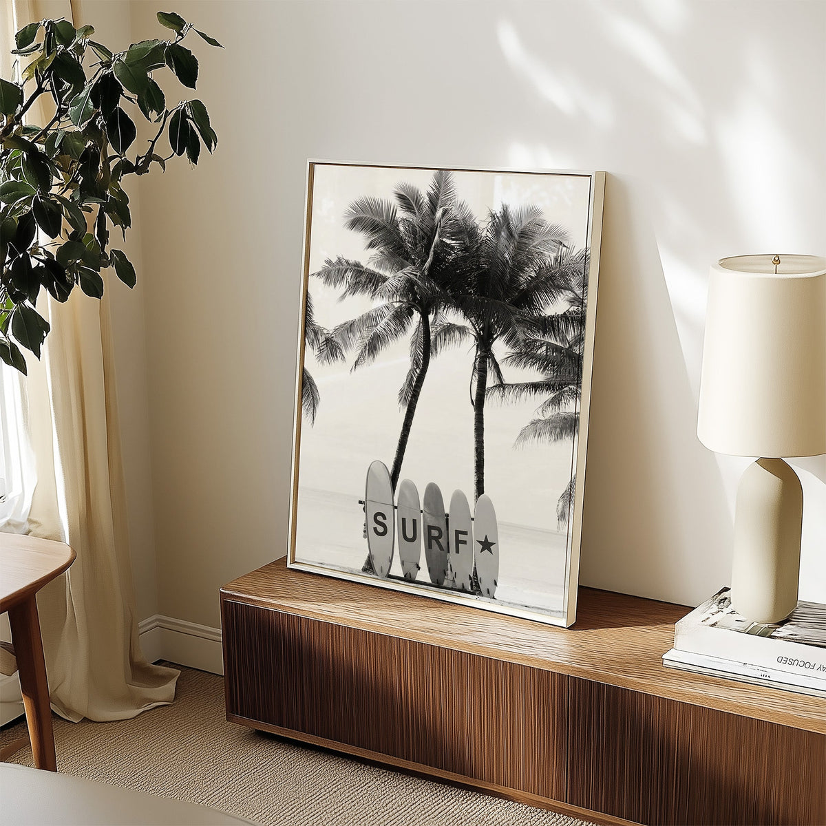 Five surfboards spelling SURF under coconut palms print in a white frame on a walnut sideboard beside a ceramic lamp