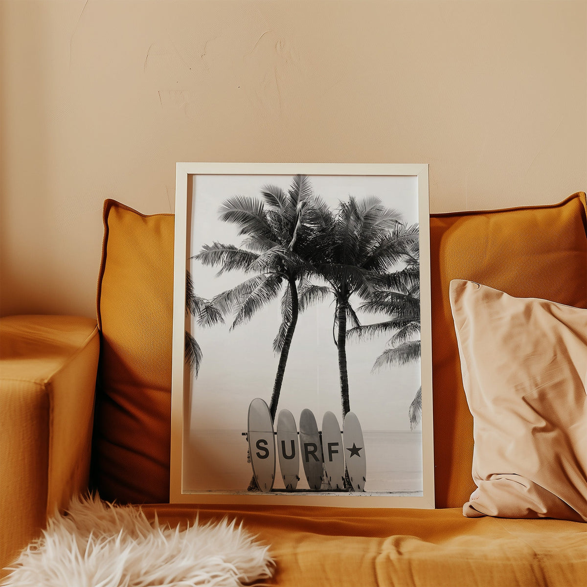 Five surfboards spelling SURF under coconut palms print in a white frame leaning on a mustard velvet sofa
