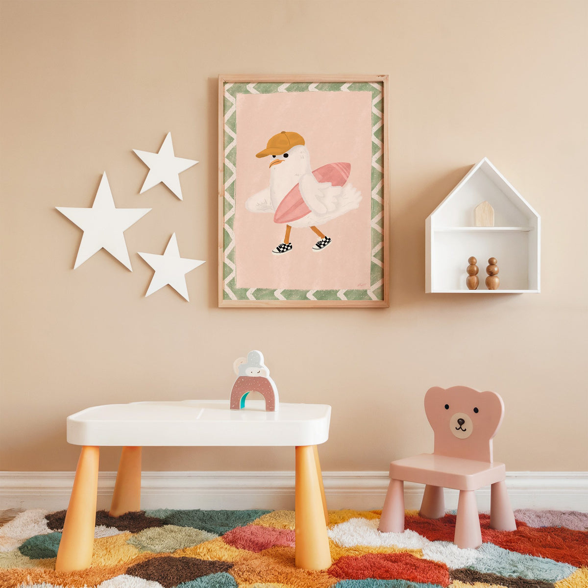 Surfer seagull with pink surfboard nursery print in an oak frame on a peach wall above a kids table with wall stars