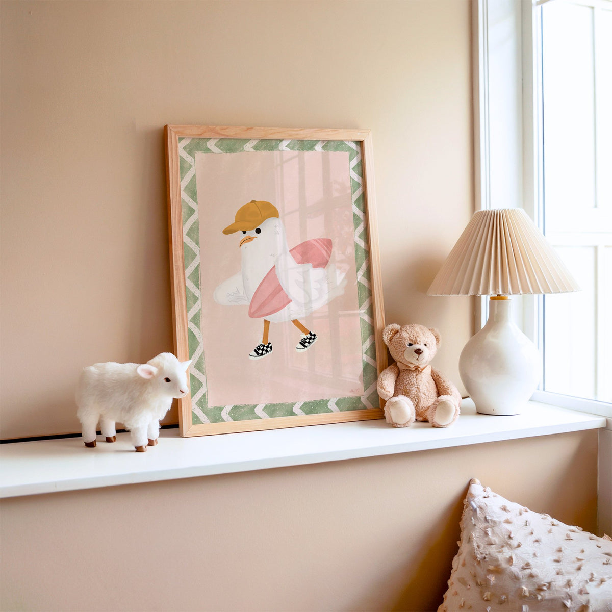 Surfer seagull with pink surfboard nursery print in an oak frame on a window ledge with a toy lamb and teddy